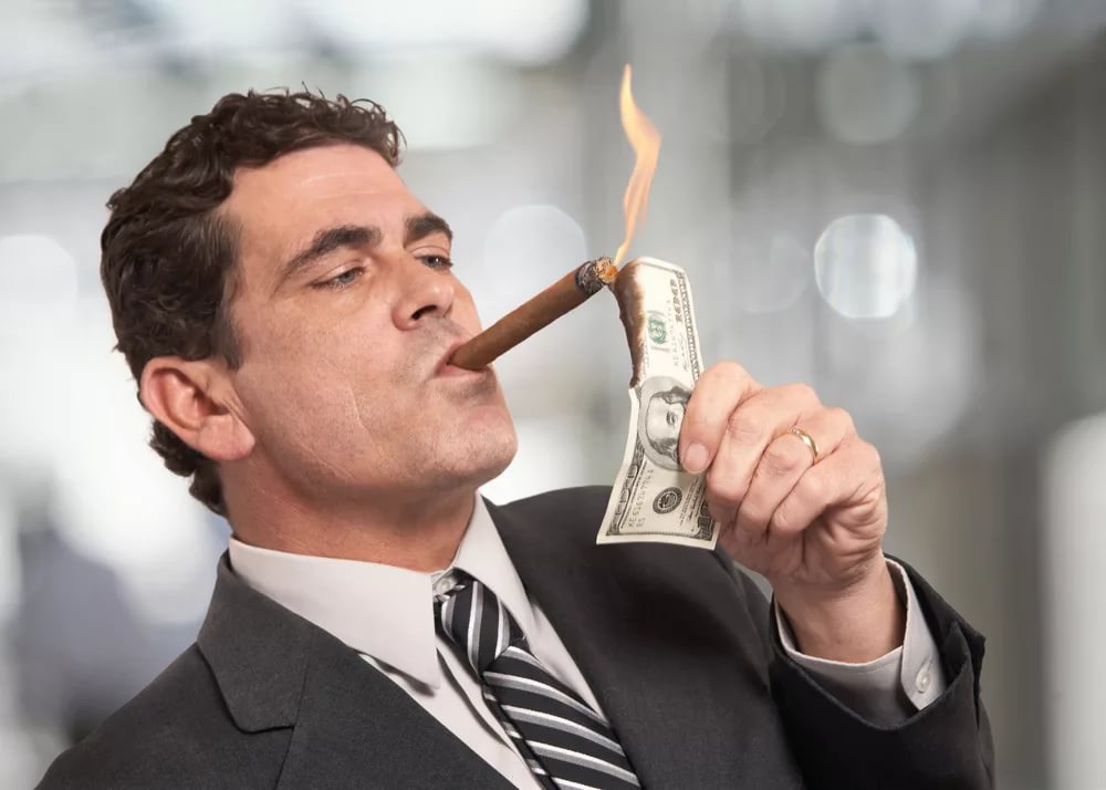 Мужчина подкуривает сигару от горящей долларовой купюры