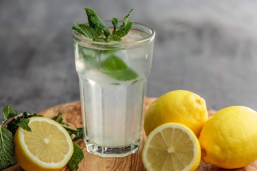 A glas of lemon water with peppermint leaves on a wooden tray
