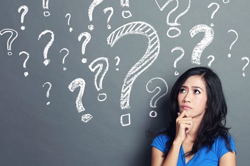 Woman standing in front of a cloud of question marks on a chalkboard.