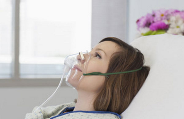 Женщина лежит в больнице с кислородной маской на лице