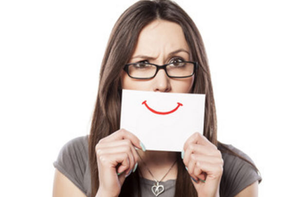 Женщина с серьезным выражением лица, которая держит перед губами листок с улыбкой