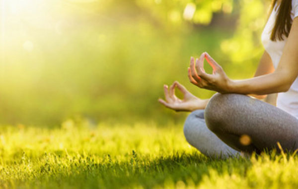 Женщина занимается медитацией, сидя на траве
