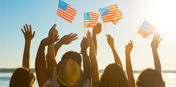 A group of young people facing the sun and waving small American flags.