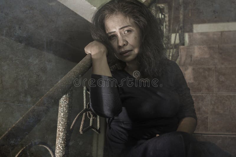 Dramatic portrait of 50s woman depressed on staircase - mature lady sad and lonely suffering depression and middle age crisis. Sitting on stairs feeling royalty free stock photography
