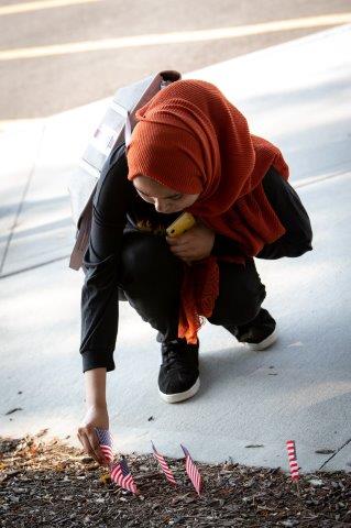 A young lady kneels down to place her American flag in the soil.