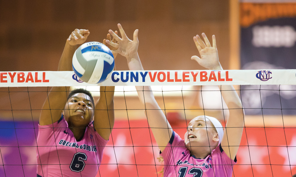 2 QCC Women's Vollyeball players reaching for the ball by the net